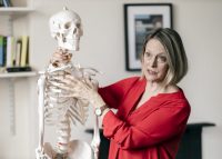 Teacher stood next to skeleton with her hand around its neck and other hand on its chest