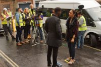 Image of actors and crew in the street wearing hi viz and stood around a camera