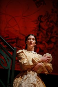 Actor on stage, in Edwardian dress, holding a baby