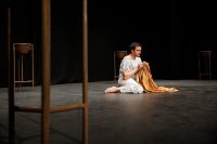 Actor sat on stage in white robes holding gold cloak