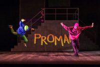 Two actors in brightly coloured shells suits and balaclavas are breakdancing on stage with graffiti artwork behind them on the set